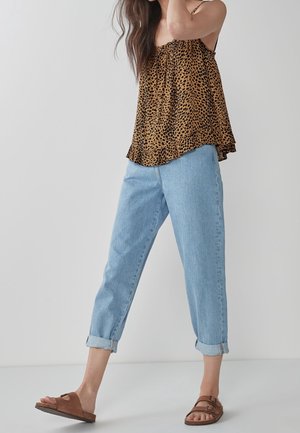 Ärmelloses Top mit Leopardenmuster in Braun und Schwarz, kombiniert mit hellblauen Jeans mit hochgekrempeltem Saum und braunen Sandalen.