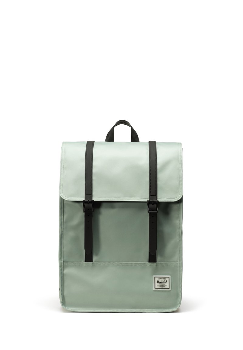 Sac à dos vert menthe avec un rabat pliable, des bretelles et des éléments en métal noirs, de forme rectangulaire, et une étiquette à l'avant indiquant la marque.