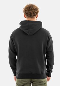 Sudadera con capucha negra, mezcla de algodón, con un ajuste relajado. Presenta un bolsillo tipo canguro y puños de canalé, vista desde la parte trasera.