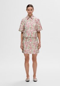 Ensemble à imprimé floral comprenant un haut à col et manches courtes, ainsi qu'une mini jupe, en rose, vert et blanc. Le tissu a une texture lisse.