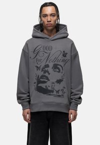 Felpa grigia oversize realizzata in materiale morbido, caratterizzata da una grande stampa grafica di un volto, farfalle e il testo "Good For Nothing."