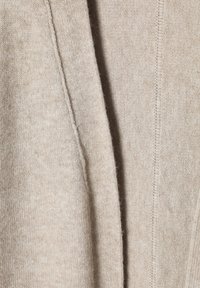 Pull beige doux fabriqué en tissu tricoté, avec une texture lisse, un léger motif côtelé et des coutures nettes le long des bords.