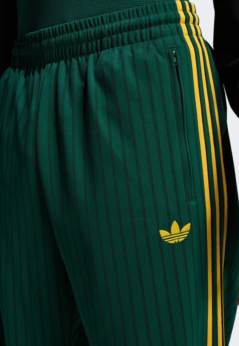 Pantalon de sport à rayures vertes avec une taille élastique, agrémenté d'accents jaunes, d'une poche zippée et d'un logo brodé.