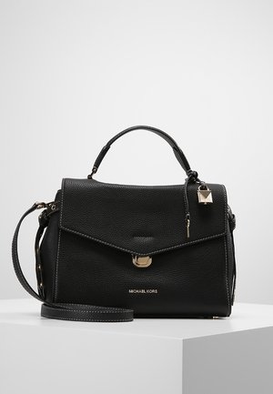 Czarna teksturowana skórzana torebka Michael Kors z górnym uchwytem, odpinanym paskiem na ramię, złotym zapięciem i dekoracyjnym breloczkiem w kształcie zamka, na białym tle.
