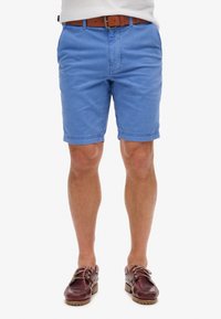 Pantaloni corti in cotone azzurro chiaro con una vestibilità rilassata, dotati di tasche anteriori e cuciture ordinate, abbinati a scarpe da barca in pelle marrone.