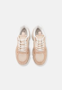 Paire de baskets beige et blanches avec des détails en mesh et en suède, lacets blancs et col rembourré, vues de dessus sur un fond clair.
