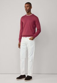 Pull rouge à manches longues avec col rond, associé à un jean droit blanc et des chaussures en suédine foncée. Design simple et épuré.