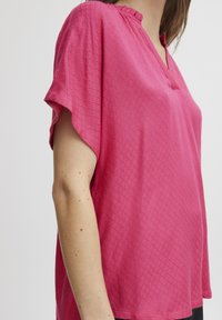 Top rosa a maniche corte con un motivo a diamante testurizzato, dotato di scollatura a V e orlo arricciato lungo il collo, vestibilità casual.