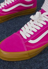 Pink canvas sneakers with a white side stripe, featuring raised rubber soles and laces. The toe and accents are a deep magenta color.