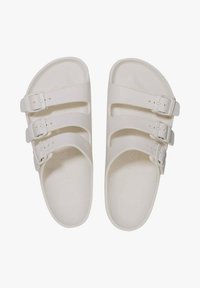 Sandali bianchi con tre cinturini regolabili, realizzati in materiale liscio, dotati di una soletta imbottita e un design minimalista.