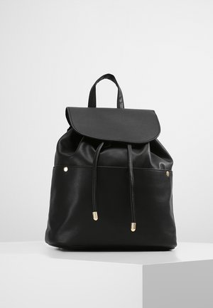 Mochila de cuero negro con solapa plegable, cierre de cordón, bolsillo frontal y acentos de hardware en tono dorado. Textura suave y forma estructurada.
