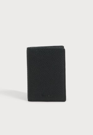 Un portefeuille GANT noir en cuir texturé est posé à la verticale sur une surface claire, devant un arrière-plan uni.