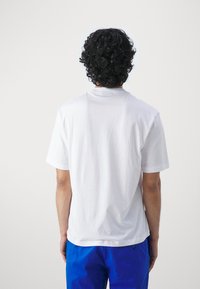 Camiseta de algodón blanca con un ajuste relajado, mangas cortas y escote redondo, presentada sobre un fondo claro.