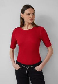 Rode geribbelde top met korte mouwen en een ronde halslijn, met een gestructureerde pasvorm. Gecombineerd met zwarte broek en handen in de zakken.