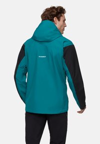 Teal en zwarte buitenjas met capuchon, voorzien van een ritszak aan de zijkant en een logo op de achterkant. Glad textuur en sportieve snit.