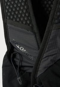 Κοντινό πλάνο μαύρης τιράντας σακιδίου Salomon με επένδυση από δίχτυ, ρυθμιζόμενο ελαστικό κορδόνι και υφή υφάσματος.