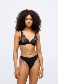 Black lace bra with floral pattern and soft cups, paired with a matching black lingerie bottom. Smooth texture, adjustable straps.