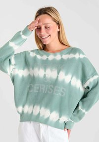 Groene en witte tie-dye oversized sweater met een ribbelstructuur en "ROCK & CERISES" in lichte letters op de voorkant. Lange mouwen.