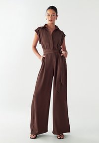 Bruine, losvallende jumpsuit met korte mouwen, kraag, knopen aan de voorkant en een strikceintuur in de taille. Glad stof met wijd uitlopende broekspijpen.
