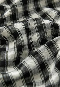 Tissu à carreaux noir et blanc avec une texture tissée, présentant des lignes épaisses et fines alternées formant un motif à carreaux.