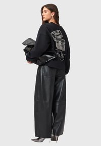 Felpa nera oversize con design grafico sulla schiena, abbinata a pantaloni in ecopelle neri lucidi a vita alta e una clutch nera.