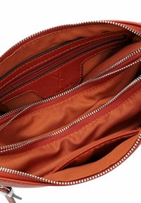 Red leather handbag interior with multiple compartments, bronze zippers, and smooth fabric lining. Features card slots and zipper pockets.