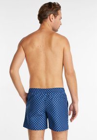 Shorts de bain à motifs bleus avec un design géométrique, taille élastique et deux poches latérales. Le tissu semble léger et texturé.