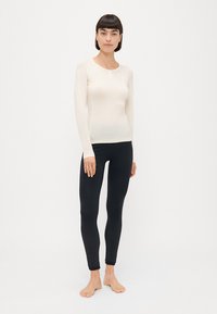 Haut crème à manches longues avec un col rond et des manches raglan, associé à un legging noir ajusté avec un motif texturé.