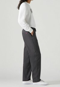 Šedé tepláky s elastickým pasem a bočními kapsami, vyrobené z měkkého materiálu. V kombinaci s bílou košilí s dlouhým rukávem a teniskami.