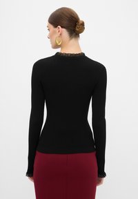 Zwarte ribbed long sleeve top met een gestructureerde kraag en franje-mouwen, gecombineerd met een bordeauxrode rok. Geen zichtbare logo's of patronen.
