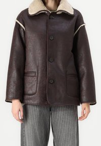 Ruskea keinonahkainen takki, jossa on beige karvahvuoreinen kaulus, napit edessä, kaksi sivutaskua ja rento istuvuus. Pinta on teksturoitu ja siinä on sävyeroja.