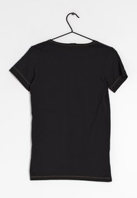 Svart bomull t-shirt med korta ärmar, med synlig gul sömnad längs kragen och ärmarna, hängande på en svart galge.