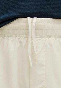 Cremefarvede træningsshorts har en elastisk talje med hvide snore og sidelommer, og de er parret med en mørkeblå struktureret top.