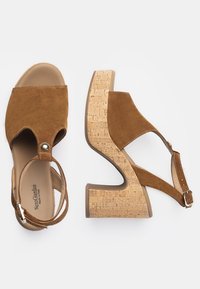 Sandali con zeppa in suede marrone e tacco in sughero. Presentano una punta aperta, una cinghia alla caviglia con fibbia e una superficie in sughero testurizzato.