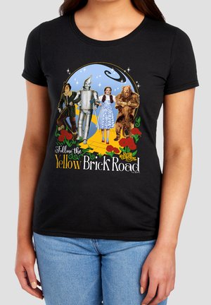 Characters from The Wizard of Oz—Scarecrow, Tin Man, Dorothy, and Cowardly Lion—walk along the yellow brick road with a night sky background.