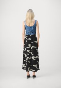 Top corto in denim con un design attillato, abbinato a una gonna maxi nera con motivi astratti bianchi. Indossato con scarpe con tacco nere.