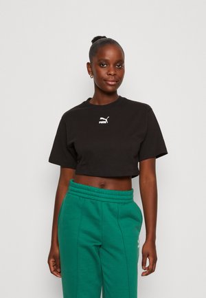 Black cropped t-shirt made of cotton, featuring a white Puma logo on the chest. Paired with green sweatpants with a stretchy waistband.