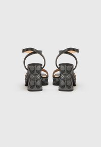 Μαύρες σανδάλια με ψηλό τακούνι και υφασμάτινο διχτυωτό επάνω μέρος, λουράκι αστραγάλου και κλείσιμο με αγκράφα. Το χοντρό τακούνι έχει στρογγυλά, ανάγλυφα σχέδια.