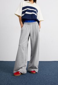 Kotníková polo košile s námořnickými a bílými pruhy, spárovaná se šedými volnými tepláky. Červené a hnědé tenisky dotvářejí celý outfit.