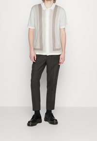 Korte mouw blouse met een crème basis en bruine verticale strepen. Gecombineerd met slim-fit donkere broeken en zwarte schoenen.