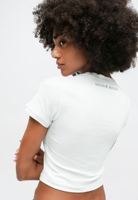 Balts īsais krekls ar īsām piedurknēm, mīksts audums, ar nenovērojamu logo izšuvumu mugurpusē netālu no kakla.