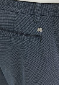 Donkerblauwe geruite broek met een fijn rasterpatroon. Voorzien van een achterzak en een klein metalen logo op de tailleband. Strak ontwerp.