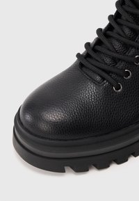 Juodas odinis botas su tekstūruotu paviršiumi, apvali noselė ir juodos raišteliai. Turi storą, tvirtą gumos padą, užtikrinančią sukibimą.
