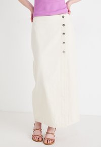 Jupe maxi en lin blanc avec un détail de boutons sur le devant, comprenant six boutons en argent sur le côté et un design droit.