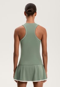Sportos ruha tompa zöld színben, amely illeszkedő felsőrésszel, bővülő szoknyával és kontrasztos fehér díszítéssel rendelkezik a nyakrésznél és a szegésnél.