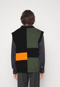 Sudadera sin mangas de punto que presenta bloques de color negro, verde y naranja, con un cuello acanalado, tela texturizada y un dobladillo recto.