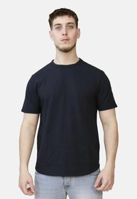 T-shirt in cotone nero con maniche corte e scollatura rotonda. Design semplice, senza motivi o logo visibili. Indossato con jeans azzurri chiari.