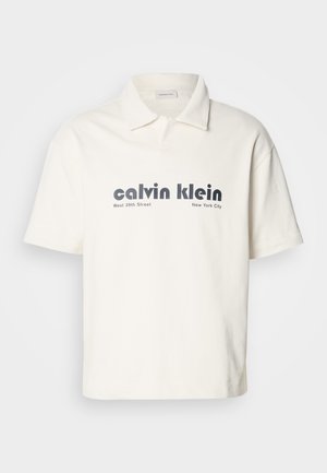 Kremo spalvos polo marškinėliai su trumpomis rankovėmis, pasižymintys kontrastinga tamsiai pilka "calvin klein" logotipu ir tekstu, pagaminti iš glotnaus medvilninio audinio.