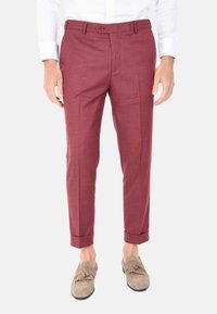Pantaloni su misura color marsala con finitura testurizzata, dotati di chiusura con un solo bottone, tasche laterali e orli arrotolati. Abbinati a mocassini grigio chiaro.