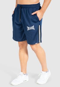 Pantalones cortos deportivos de color azul marino con textura acanalada, cinturilla elástica, bolsillos laterales, logo blanco y detalles a rayas en los lados.